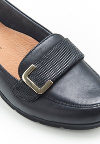 Zapato de cuero negro con una correa texturizada y hebilla en tono dorado. Presenta una suela de perfil bajo y un interior acolchado para mayor comodidad.