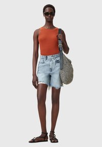 Oranje tanktop, versleten lichtdenim shorts, zwarte platte sandalen en een gestreepte tas met een lange schouderband. Accessoires omvatten een zonnebril.