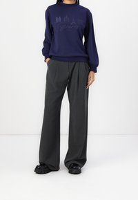 Sweat-shirt bleu marine avec un graphisme de Paris, assorti à un pantalon gris taille haute à jambes larges et à des chaussures noires à plateforme. Texture de tissu lisse.