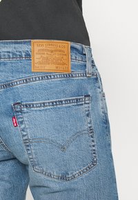 Ljust blå denimjeans med en läderbaksida märkt "Levi Strauss & Co." och en synlig röd etikett på bakfickan. Klassisk femficksdesign.