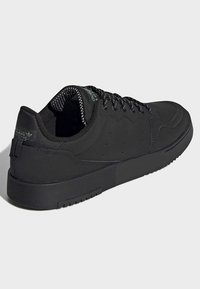 Scarpe sportive nere con tomaia in sintetico liscio, fodera in rete testurizzata, lacci piatti e suola in gomma spessa, caratterizzate da sottili perforazioni.