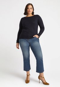 Granatowy sweter dzianinowy z długimi rękawami i guzikami, w połączeniu z niebieskimi dżinsami o średnim stanie i brązowymi lakierowanymi szpilkami.