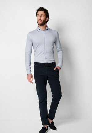 Helles blaues Langarmhemd mit Knöpfen, kombiniert mit dunkelblauen Hosen und dunklen Slippern, im Slim Fit Design und mit strukturiertem Stoff.
