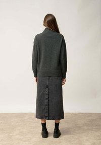 Ciemnoszary sweter dziany z wysokim kołnierzem, zestawiony z czarną dżinsową spódnicą o długości midi z tylnym szwem oraz czarnym obuwiem.