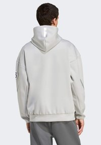 Hellgrauer Hoodie mit hohem Kragen, Reißverschlussdetails und gerippten Bündchen. Verfügt über einen reflektierenden Streifen auf der Kapuze und ein Logo auf dem Ärmel.