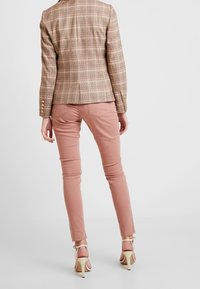 Blazer à carreaux dans des tons beige et rose avec des boutons dorés, associé à un pantalon rose clair ajusté et des sandales à talons haut beige.