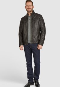 Schwarze Lederjacke mit Stehkragen, Reißverschluss vorne und Taschen. Getragen über einem grauen Hemd und kombiniert mit dunklen Jeans und schwarzen Schuhen.