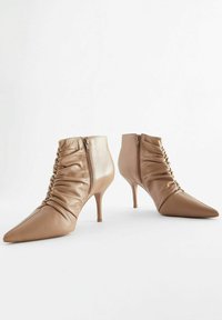 Bottines en cuir tan avec des pointes effilées et des détails froncés. Comprend une fermeture éclair sur le côté et un talon fin de 7,5 cm. Texture lisse.