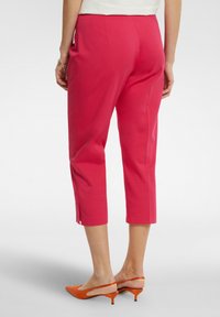Pantaloni capri rosa realizzati in tessuto liscio, caratterizzati da un design aderente e fessure laterali all'orlo. Abbinati a tacchi slingback arancioni.