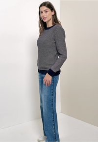 Marineblau und weiß gemusterter Pullover mit langen Ärmeln, geripptem Kragen und Bündchen, kombiniert mit hellblauen Straight-Leg-Jeans und weißen Sneakern.