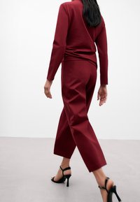 Top bordeaux e pantaloni a gamba larga coordinati, entrambi in tessuto morbido. L'outfit presenta maniche lunghe e una vestibilità rilassata, abbinato a sandali con tacco alto.
