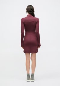 Vinröd figurnära klänning med långa ärmar, hög krage och en elegant design; tillverkad av mjukt tyg och med längd som når mitten av låret.