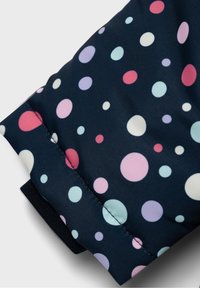 Gros plan sur un tissu en rembourrage bleu marine avec des pois pastel en rose, violet, bleu clair et blanc, montrant les détails de couture.