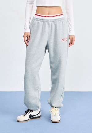 Szare spodnie dresowe o luźnym kroju, z elastycznym pasem i bocznymi rozcięciami, w połączeniu z czarno-białymi trampkami z żółtymi sznurowadłami.