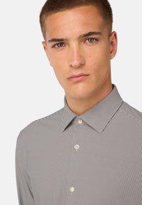 Camicia abbottonata grigia con sottili righe verticali; presenta un colletto standard e due chiusure con bottoni sul davanti.
