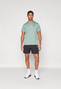 Camiseta atlética verde claro de manga corta, combinada con pantalones cortos negros y zapatillas blancas con acentos rojos. Logo de Puma en ambas prendas.