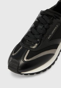 Μαύρο και γκρι αθλητικό παπούτσι Karl Lagerfeld με επάνω μέρος από δίχτυ και δέρμα, μαύρα κορδόνια και λευκή σόλα με ανάγλυφο για καλύτερη πρόσφυση.