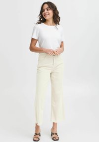 White short-sleeve t-shirt paired with high-waisted, light beige wide-leg pants and black strappy heeled sandals. Smooth fabric, casual fit.