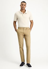 Beige polo shirt and tan slim-fit trousers with a smooth texture, paired with navy slip-on shoes and a simple button detail on the collar.