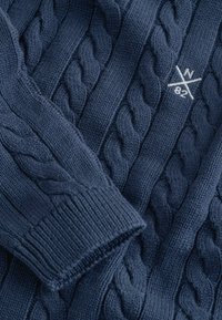 Tumesinise värvusega kaablis kudumiga kampsun, mis sisaldab tekstuuriga mustreid, soonikkoes varrukaotsi ja väikest valget tikandiga logot kangal.