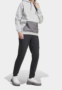 Šedá mikina s kapucí a tmavě šedou přední kapsou, spárovaná s černými kalhotami s bočními zipovými kapsami a bílými teniskami s šedými akcenty.