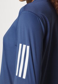 Marineblaues Sportshirt mit strukturierter Stoffqualität und Mesh-Akzenten an den Schultern. Weiße Drei-Streifen-Markenkennzeichnung am Ärmel.