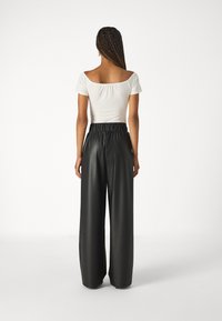 White off-the-shoulder top and high-waisted black faux leather wide-leg pants, featuring an elastic waistband and smooth texture.