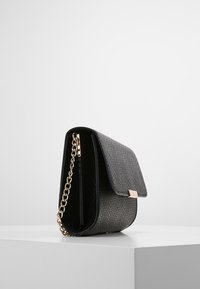 Černá texturovaná kabelka s překlopným klopovým víkem, zlatými detaily a řetízkovým popruhem. Tělo má strukturovaný tvar a jemný vzor.