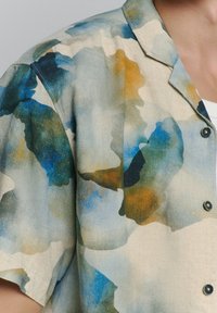 Korte mouwen shirt van lichte stof met een abstract aquarelpatroon in blauw, groen en oranje tinten; inclusief zwarte knopen.