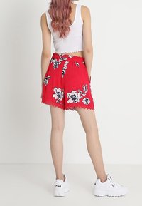 Rode bloemen short met een golvende zoom, een cinched tailleband en een wit bloemenpatroon. Draagt het met een witte crop top en witte sneakers.