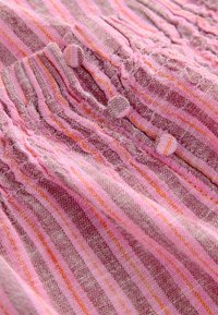 Tissu rayé rose et orange avec une partie froncée et quatre boutons recouverts placés verticalement le long de la texture.