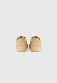Tan mockaskinnsneakers med rund tå, flat gummisåle og fremtredende sømmer. Bakdelen har en polstret krage og slip-on design.