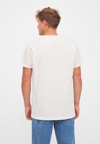 Hvid bomulds t-shirt med korte ærmer, lige kant og en afslappet pasform. Båret med blå denim jeans. Bagfra, minimal tekstur synlig.