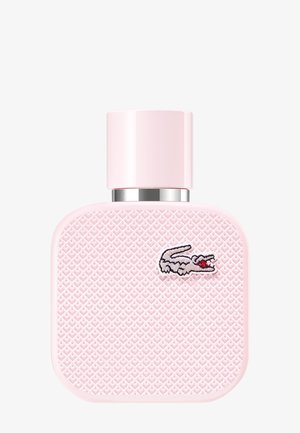 Flacon de parfum carré rose clair avec surface texturée et petit logo crocodile brodé près du coin supérieur droit.