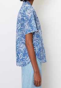 Camicia a maniche corte blu con motivo floreale che presenta schemi botanici bianchi, una vestibilità relax e un orlo curvo, realizzata in tessuto leggero.