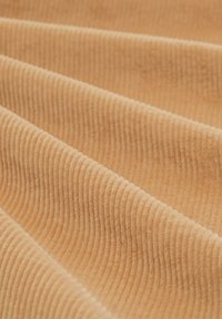 Tissu côtelé texturé de couleur pêche douce, présentant des ridules parallèles. Le matériau semble moelleux avec une légère brillance. Les plis créent de la profondeur.