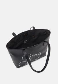 Mustat nahkataskut, joissa on valkoinen Mikki Hiiri -printti, avoin yläosa, kaksi kahvaa ja yksi sisäinen vetoketjullinen tasku. Pehmeätekstuurinen ja tilava sisustus.