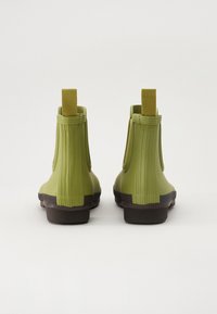 Botas de goma verdes hasta el tobillo con estrías verticales, lengüetas en la parte superior y suelas marrones; diseño resistente adecuado para condiciones húmedas.