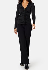 Czarny longsleeve z marszczonymi detalami i zapięciem na guziki, w zestawieniu z czarnymi spodniami o szerokich nogawkach i botkami za kostkę. Gładki, elastyczny materiał.