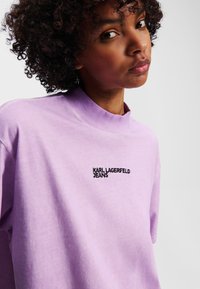 Lys lilla oversized bomull t-skjorte med høy hals og korte ermer. Har et svart brodert "KARL LAGERFELD JEANS" logo.
