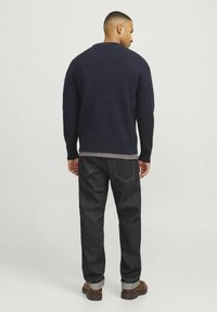 Dunkelblauer gerippter Pullover mit Rundhalsausschnitt, kombiniert mit dunklen Jeans. Hellbraune Schuhe und hochgekrempelte Hosenbeine runden den Look ab.