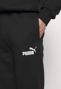 Black sweatpants made of soft fabric, featuring a white Puma logo on the left leg, with a regular fit and side pockets.