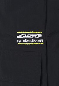 Tecido preto com acabamento texturizado. Apresenta um logótipo da Quiksilver em branco e amarelo com acentos em ziguezague. Inclui um bolso frontal.