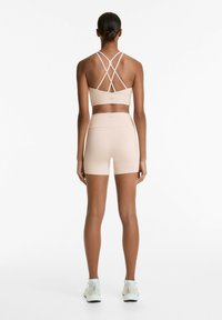Ljusrosa sport-bh med korslagda axelremmar och matchande högmidjade shorts. En slät yta framhäver den eleganta designen.