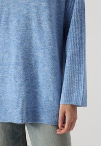 Pull bleu clair fabriqué en matériau doux, doté de poignets et d'un ourlet côtelés, et d'une coupe décontractée. Associé à un jean en denim clair.