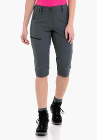 Pantalones cortos grises hasta la rodilla con un bolsillo con cremallera, fabricados en tela ligera. Combinados con botas de senderismo negras y calcetas grises.