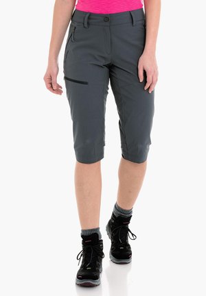Pantalones cortos grises hasta la rodilla con un bolsillo con cremallera, fabricados en tela ligera. Combinados con botas de senderismo negras y calcetas grises.