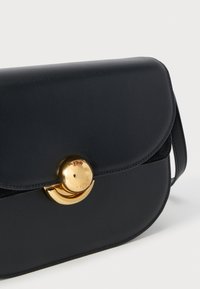 Sort læder crossover-taske med rundet klap og guld rundlås, vist mod en ensartet hvid baggrund.