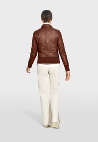 Brun läderbomberjacka med ribbade ärmslut, krage och en figursydd design, ihop med ljusbeiga vida byxor och beiga skor.