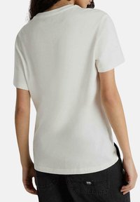 Camiseta blanca de manga corta con cuello redondo, hecha de una tela suave. La prenda presenta un dobladillo que se curva ligeramente a los lados.